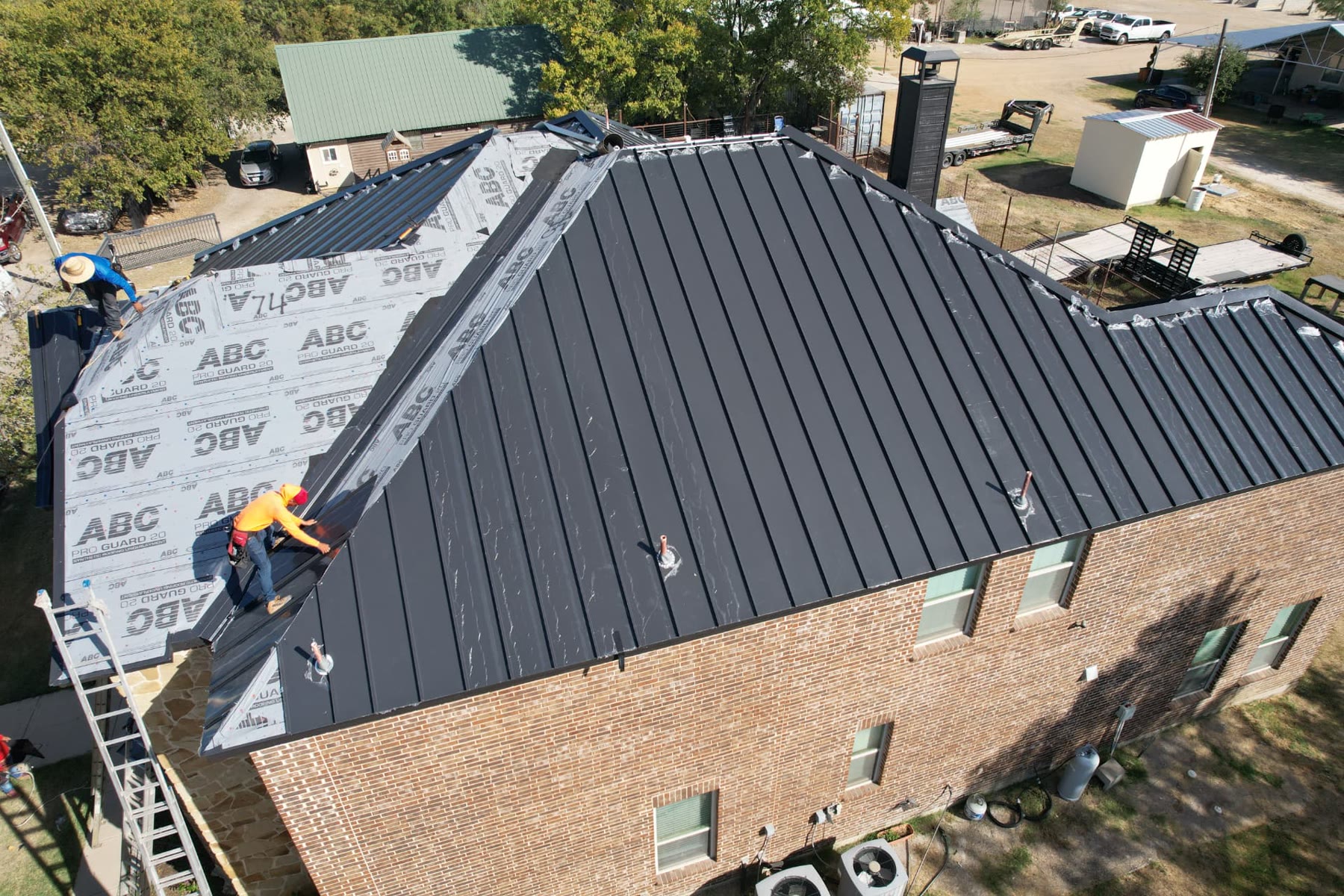 Crew installing a black standing seam metal roof over synthetic underlayment on a North Texas brick home